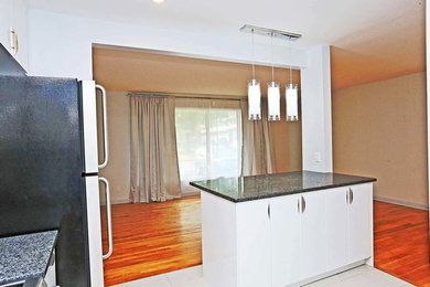 Mid-sized trendy l-shaped ceramic tile enclosed kitchen photo in Ottawa with a single-bowl sink, flat-panel cabinets, white cabinets, granite countertops, white backsplash, glass tile backsplash, stainless steel appliances and an island