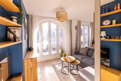 Diseño de salón abierto moderno de tamaño medio con paredes azules, suelo de madera clara y televisor independiente