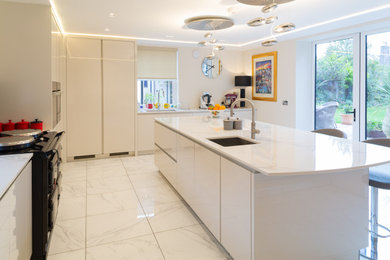 Inspiration for a large l-shaped kitchen/diner in Edinburgh with flat-panel cabinets, white cabinets, composite countertops, white splashback, integrated appliances, ceramic flooring, an island, white floors and white worktops.
