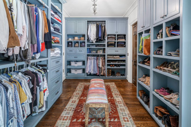 Modelo de armario vestidor de estilo de casa de campo grande con armarios con paneles empotrados, puertas de armario azules, suelo de madera en tonos medios y suelo marrón