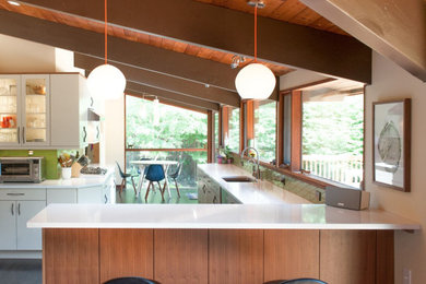This is an example of a midcentury eat-in kitchen in Philadelphia with an undermount sink, flat-panel cabinets, quartz benchtops, green splashback, stainless steel appliances, a peninsula, brown floor and white benchtop.