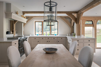 Photo of a large country u-shaped open plan kitchen in Surrey with an undermount sink, recessed-panel cabinets, beige cabinets, granite benchtops, beige splashback, limestone floors, black appliances and a peninsula.