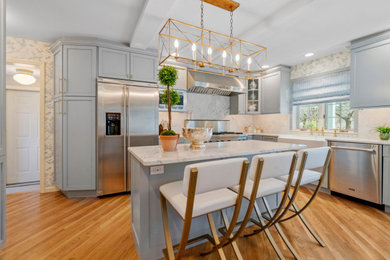 Large elegant u-shaped light wood floor and brown floor kitchen photo in New York with a farmhouse sink, recessed-panel cabinets, blue cabinets, marble countertops, white backsplash, marble backsplash, stainless steel appliances, an island and white countertops
