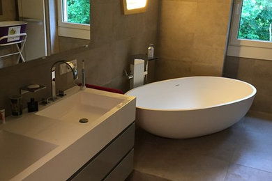 Mittelgroßes Modernes Duschbad mit flächenbündigen Schrankfronten, grauen Schränken, freistehender Badewanne, Steinfliesen, grauer Wandfarbe, Betonboden, integriertem Waschbecken, weißer Waschtischplatte, bodengleicher Dusche, Wandtoilette mit Spülkasten, beigen Fliesen, Mineralwerkstoff-Waschtisch, beigem Boden und offener Dusche in Köln