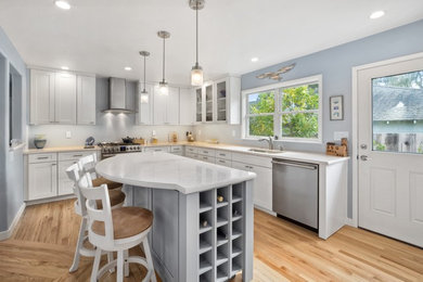 Example of a mid-sized trendy medium tone wood floor and brown floor kitchen design with an undermount sink, shaker cabinets, white cabinets, solid surface countertops, stainless steel appliances and an island