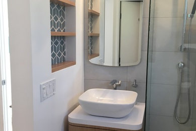 Corner shower - small contemporary master white tile and porcelain tile porcelain tile and white floor corner shower idea in Santa Barbara with furniture-like cabinets, light wood cabinets, white walls, a vessel sink, quartzite countertops and a hinged shower door