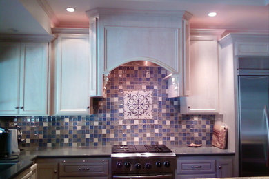Example of a trendy l-shaped kitchen design in Other with an undermount sink, recessed-panel cabinets, white cabinets, blue backsplash, ceramic backsplash, stainless steel appliances and an island