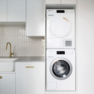 Inredning av en maritim stor grå linjär grått tvättstuga enbart för tvätt, med en nedsänkt diskho, luckor med upphöjd panel, vita skåp, granitbänkskiva, beige stänkskydd, stänkskydd i tunnelbanekakel, beige väggar, klinkergolv i keramik, en tvättpelare och beiget golv
