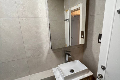 Photo of a medium sized modern family bathroom in London with flat-panel cabinets, dark wood cabinets, a walk-in shower, a wall mounted toilet, beige tiles, stone tiles, beige walls, terracotta flooring, a wall-mounted sink, tiled worktops, beige floors, a hinged door, grey worktops, feature lighting, a single sink and a floating vanity unit.