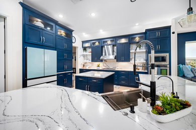 Example of a large trendy eat-in kitchen design in Austin with a farmhouse sink, shaker cabinets, blue cabinets, quartz countertops, white backsplash, stainless steel appliances, two islands, white countertops and quartz backsplash