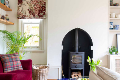 This is an example of a small eclectic enclosed living room curtain in West Midlands with white walls, medium hardwood flooring, a wood burning stove, a plastered fireplace surround, a wall mounted tv and brown floors.