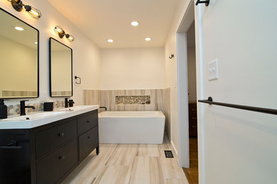 Design ideas for a mid-sized industrial master bathroom in Raleigh with flat-panel cabinets, black cabinets, a freestanding tub, a curbless shower, a two-piece toilet, multi-coloured tile, porcelain tile, white walls, porcelain floors, an integrated sink, solid surface benchtops, multi-coloured floor, an open shower and white benchtops.