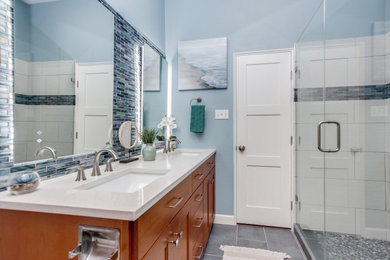 Photo of a medium sized nautical family bathroom in Dallas with shaker cabinets, medium wood cabinets, an alcove shower, a two-piece toilet, multi-coloured tiles, porcelain tiles, blue walls, porcelain flooring, a submerged sink, engineered stone worktops, grey floors, a hinged door, white worktops, a wall niche, double sinks and a freestanding vanity unit.