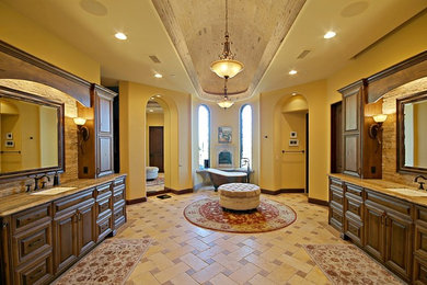 Freestanding bathtub - large mediterranean master beige tile and stone tile travertine floor freestanding bathtub idea in Phoenix with raised-panel cabinets, medium tone wood cabinets, yellow walls, an undermount sink and granite countertops