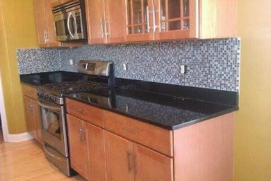 Elegant light wood floor kitchen photo in Milwaukee with medium tone wood cabinets, black backsplash and stainless steel appliances
