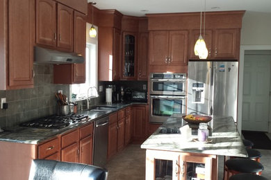 Open concept kitchen - mid-sized traditional l-shaped open concept kitchen idea in Bridgeport with a double-bowl sink, raised-panel cabinets, medium tone wood cabinets, granite countertops, gray backsplash, paneled appliances and an island
