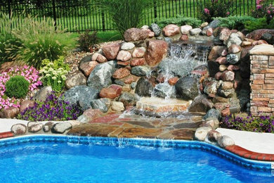 Mid-sized traditional backyard custom-shaped lap pool in St Louis with a water feature and brick pavers.