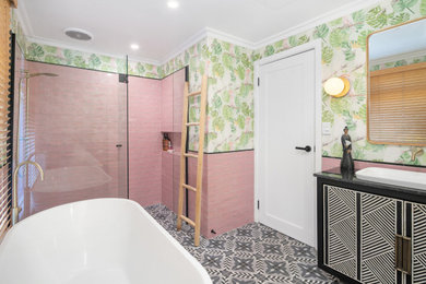 Photo of a mid-sized eclectic master bathroom in Geelong with furniture-like cabinets, black cabinets, a freestanding tub, an alcove shower, a one-piece toilet, pink tile, ceramic tile, multi-coloured walls, ceramic floors, a drop-in sink, multi-coloured floor, a hinged shower door, black benchtops, a niche, a single vanity, a built-in vanity, wallpaper and granite benchtops.
