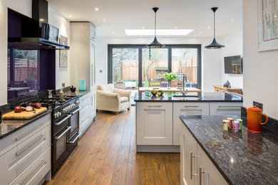 Large contemporary galley eat-in kitchen in London with an integrated sink, shaker cabinets, grey cabinets, black appliances, medium hardwood floors, with island and brown floor.