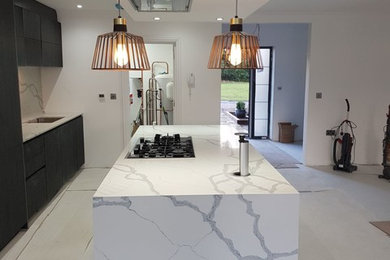 Inspiration for a large contemporary open plan kitchen in Surrey with flat-panel cabinets, grey cabinets, composite countertops, stone slab splashback and an island.