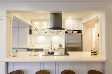 バンクーバーにある高級な中くらいなコンテンポラリースタイルのおしゃれなキッチン (エプロンフロントシンク、シェーカースタイル扉のキャビネット、白いキャビネット、クオーツストーンカウンター、白いキッチンパネル、サブウェイタイルのキッチンパネル、シルバーの調理設備、ラミネートの床、茶色い床、白いキッチンカウンター) の写真