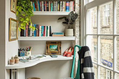 This is an example of a small contemporary home office in London with a library, grey walls, medium hardwood floors, a built-in desk and brown floor.