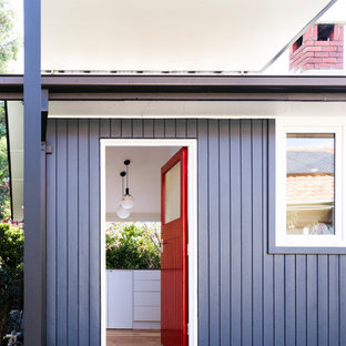 キャンベラの小さい片開きドアコンテンポラリースタイルのおしゃれな玄関ドア (無垢フローリング、赤いドア、青い壁、茶色い床) の写真