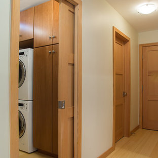 Photo of a small farmhouse single-wall utility room in San Francisco with flat-panel cabinets, medium wood cabinets, bamboo flooring, a stacked washer and dryer and yellow floors.