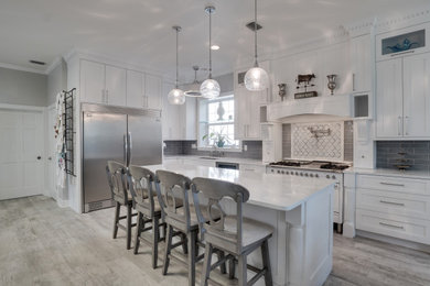 Example of a cottage l-shaped gray floor kitchen design in Orlando with an undermount sink, shaker cabinets, white cabinets, gray backsplash, white appliances, an island and white countertops