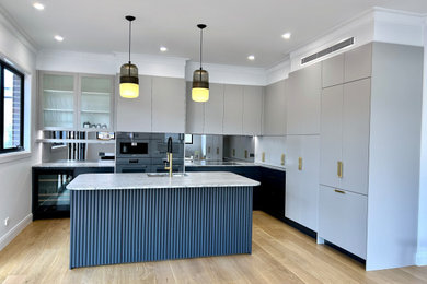 This is an example of a large transitional l-shaped eat-in kitchen in Sydney with an undermount sink, flat-panel cabinets, grey cabinets, marble benchtops, grey splashback, mirror splashback, black appliances, light hardwood floors, with island, brown floor and grey benchtop.