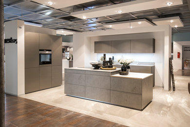 Offene Moderne Küche in L-Form mit grauen Schränken, Küchenrückwand in Weiß, schwarzen Elektrogeräten, Kücheninsel und beigem Boden in Düsseldorf