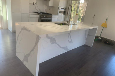 Inspiration for a contemporary eat-in kitchen remodel in New York with flat-panel cabinets, white cabinets, quartz countertops, white backsplash, quartz backsplash, stainless steel appliances, an island and white countertops