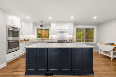 Inspiration for a mid-sized transitional u-shaped light wood floor and brown floor enclosed kitchen remodel in Atlanta with recessed-panel cabinets, white cabinets, quartz countertops, white backsplash, quartz backsplash, stainless steel appliances, an island, white countertops and an undermount sink