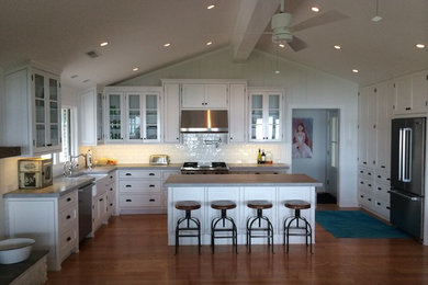 Example of a mid-sized classic l-shaped open concept kitchen design in Richmond with a farmhouse sink, glass-front cabinets, white cabinets, concrete countertops, white backsplash, porcelain backsplash, stainless steel appliances and an island
