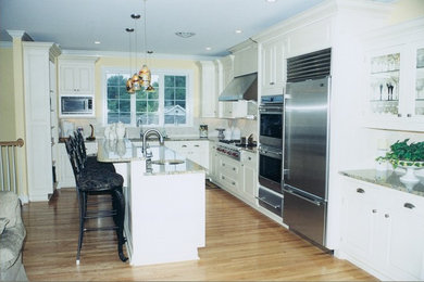 Large elegant l-shaped light wood floor open concept kitchen photo in Other with an undermount sink, beaded inset cabinets, white cabinets, granite countertops, beige backsplash, ceramic backsplash, stainless steel appliances and an island