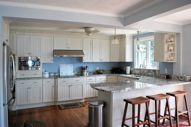 Photo of a large beach style u-shaped eat-in kitchen in Portland Maine with an undermount sink, white cabinets, granite benchtops, stainless steel appliances, dark hardwood floors, with island and beaded inset cabinets.