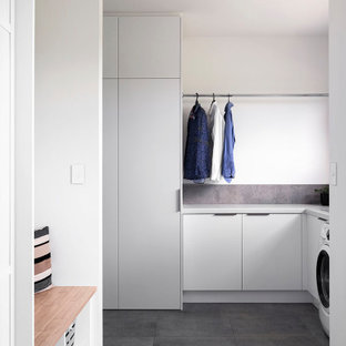 Exempel på en mellanstor modern grå l-formad grått tvättstuga enbart för tvätt, med en undermonterad diskho, släta luckor, grå skåp, bänkskiva i terrazo, grått stänkskydd, stänkskydd i keramik, vita väggar, klinkergolv i keramik, en tvättmaskin och torktumlare bredvid varandra och grått golv
