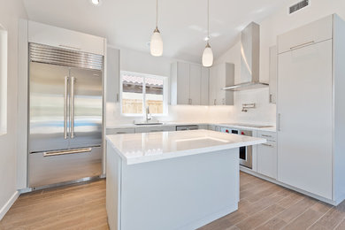 Inspiration for a mid-sized contemporary l-shaped porcelain tile and brown floor kitchen remodel in San Diego with an undermount sink, flat-panel cabinets, white cabinets, quartz countertops, white backsplash, stainless steel appliances and an island