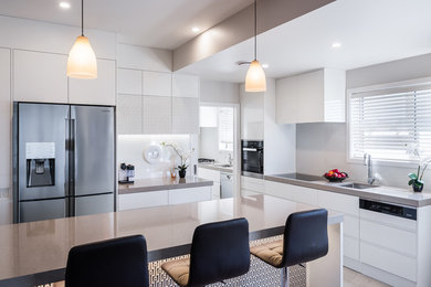 Mid-sized modern kitchen in Wellington with white cabinets, granite benchtops, white splashback, ceramic floors, with island and brown floor.