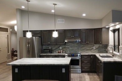 Photo of a mid-sized transitional l-shaped eat-in kitchen in Phoenix with an undermount sink, raised-panel cabinets, dark wood cabinets, granite benchtops, grey splashback, stone slab splashback, stainless steel appliances, light hardwood floors, with island and beige floor.