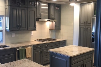 Enclosed kitchen - large transitional u-shaped travertine floor and beige floor enclosed kitchen idea in Miami with a double-bowl sink, raised-panel cabinets, gray cabinets, granite countertops, gray backsplash, glass tile backsplash, stainless steel appliances and an island