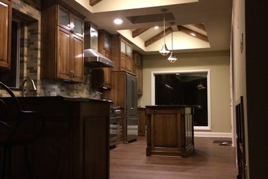 Kitchen pantry - mid-sized transitional l-shaped kitchen pantry idea in Austin with an undermount sink, raised-panel cabinets, medium tone wood cabinets, granite countertops, beige backsplash, stainless steel appliances and an island