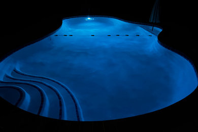 Imagen de piscina clásica de tamaño medio a medida en patio trasero con losas de hormigón