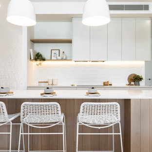 This is an example of a beach style galley kitchen in Sydney with an undermount sink, flat-panel cabinets, white cabinets, white splashback, white benchtop and with island.