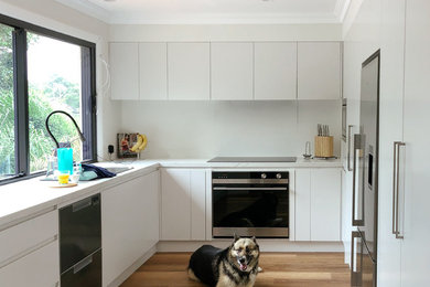 This is an example of a contemporary l-shaped eat-in kitchen in Sydney with a double-bowl sink, flat-panel cabinets, grey cabinets, quartz benchtops, grey splashback, stone slab splashback, stainless steel appliances, medium hardwood floors and grey benchtop.