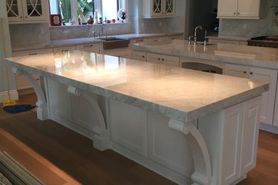 Mid-sized minimalist u-shaped medium tone wood floor enclosed kitchen photo in Miami with a farmhouse sink, shaker cabinets, white cabinets, marble countertops, white backsplash, marble backsplash, stainless steel appliances and two islands