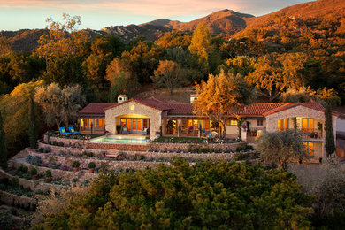 Inspiration for a large rustic beige two-story stone house exterior remodel in Santa Barbara with a tile roof and a hip roof
