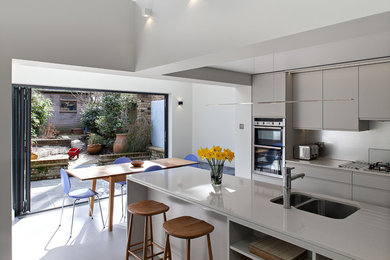 Inspiration for a large contemporary galley eat-in kitchen in London with an integrated sink, flat-panel cabinets, white cabinets, quartz benchtops, grey splashback, glass sheet splashback, panelled appliances, ceramic floors, with island, beige floor and white benchtop.