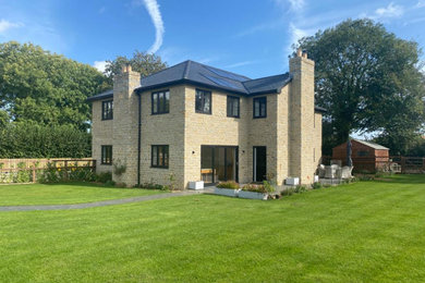 Medium sized and beige classic two floor rear detached house in Other with stone cladding, a hip roof, a tiled roof and a grey roof.