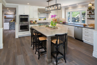 Open concept kitchen - large transitional l-shaped medium tone wood floor and brown floor open concept kitchen idea in Orange County with an undermount sink, recessed-panel cabinets, white cabinets, gray backsplash, ceramic backsplash, stainless steel appliances, an island and quartz countertops